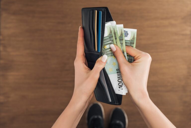 top view of woman putting euros banknotes in wallet on wooden background